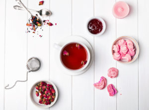 Herbal tea with dried roses, jam and small pink pastries on the white table, top view