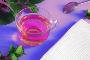 Glass cup of hot aromatic tea on pink background, neon, drink